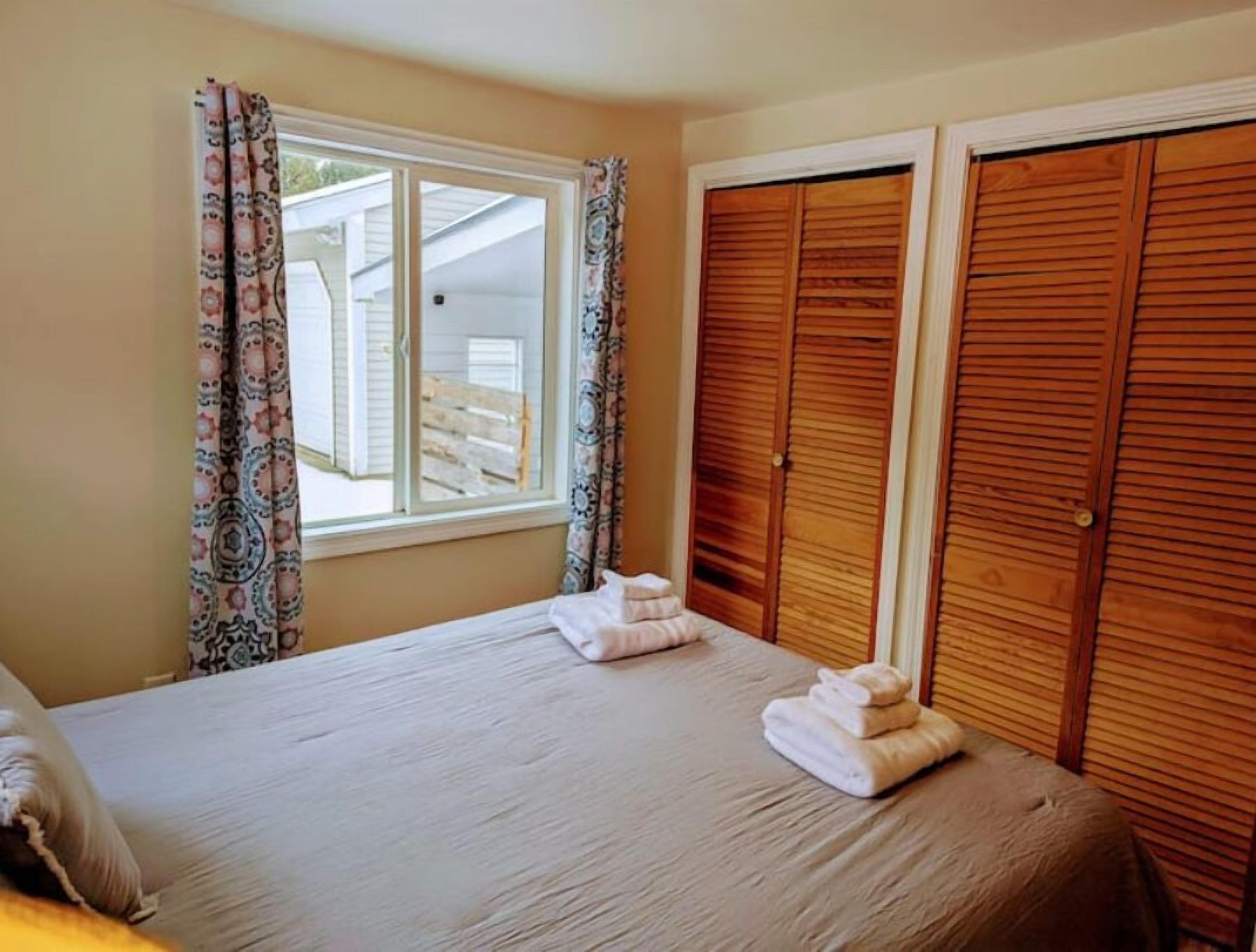 A bedroom with a bed, a window with curtains, and wooden closets.