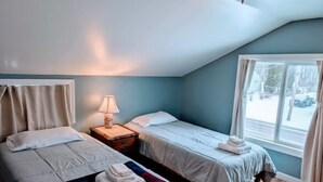 Un dormitorio con dos camas, una mesita de noche con lámpara, una ventana con cortinas y vistas al exterior.