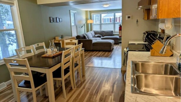 Un comedor con mesa y sillas de madera, una cocina con electrodomésticos de acero inoxidable y una sala de estar con sofá y lámpara.