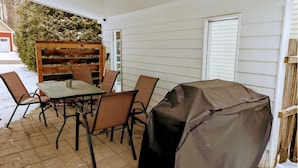 Un patio con una mesa y sillas, una parrilla cubierta y un banco de madera.