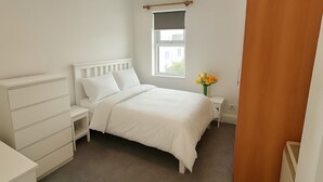 A bedroom with a bed, nightstands, a dresser, a window, and a vase with flowers. - City Centre Location - Sleeps 6 (Galway)