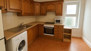 A kitchen with wooden cabinets, a washing machine, a microwave, and a window. - City Centre Location - Sleeps 6 (Galway)