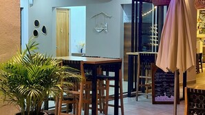 Een gezellig eetgedeelte binnen met houten tafels en stoelen, een grote potplant en hangende lichtslingers.