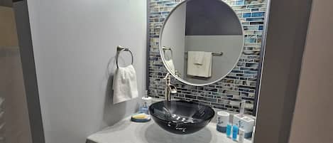 A bathroom with a round mirror, a glass sink, and a tiled backsplash.