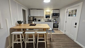 A modern kitchen with white cabinets, a wooden dining table, and four white stools. - Cozy Coastal 2-bedroom condo with AC, WiFi in welcoming Saco (Saco)