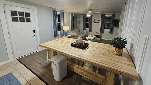 A modern living room with a wooden dining table, a sofa, and a TV mounted on the wall. - Cozy Coastal 2-bedroom condo with AC, WiFi in welcoming Saco (Saco)
