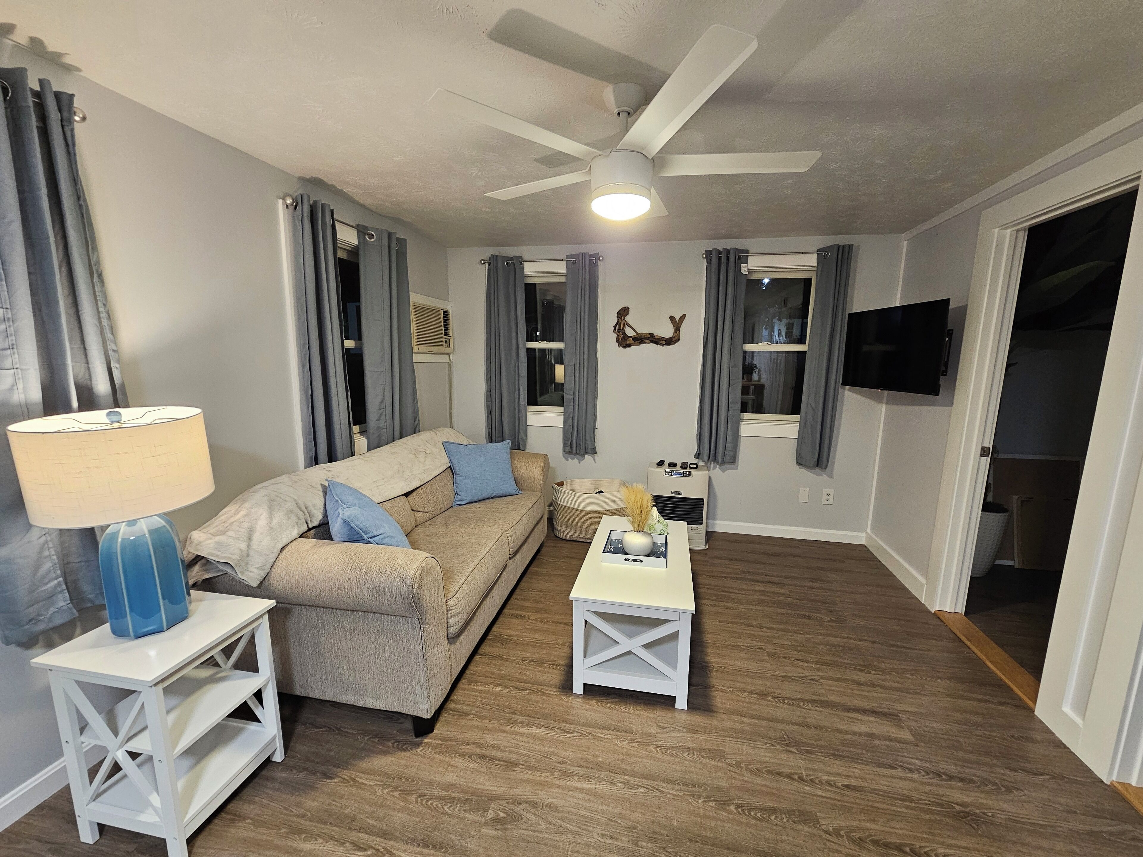 A living room with a beige sofa, a white coffee table, a lamp, and a ceiling fan.