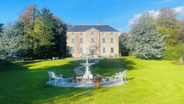 A large, historic building with a symmetrical facade, a central entrance with a portico, and a well-maintained lawn with a fountain and seating area. - Stunning historic manor house with WiFi near charming Nenagh (Nenagh)