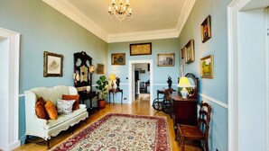 A spacious living room with a large sofa, a wooden coffee table, and a patterned rug. There are several framed pictures on the walls and a chandelier hanging from the ceiling. - Stunning historic manor house with WiFi near charming Nenagh (Nenagh)