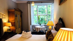 A hotel room with a bed, two bedside lamps, a wooden wardrobe, a table with chairs, and a window with a view of greenery. - Stunning historic manor house with WiFi near charming Nenagh (Nenagh)
