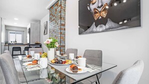 Un espace repas moderne avec une table en verre, des chaises à revêtement gris et un mur décoratif en briques.