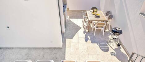 Eine Dachterrasse mit Tisch, Stühlen, einem Grill und Liegestühlen mit Handtüchern.