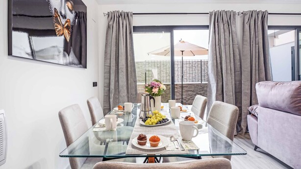 Un espace repas moderne avec une table en verre, des rideaux gris et une vue sur le balcon.
