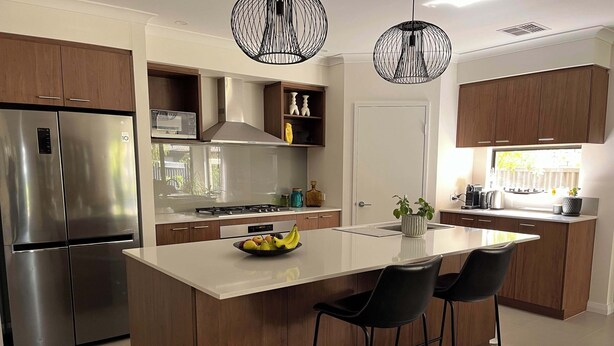A modern kitchen with a central island, stainless steel appliances, wooden cabinets, and black bar stools. - Mid-century Elegance in a leafy garden (Padbury)