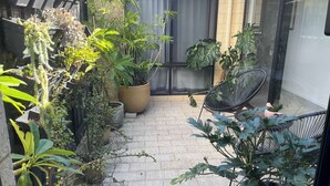 A small, enclosed outdoor space with potted plants, a black chair, and a glass door leading to a building. - Mid-century Elegance in a leafy garden (Padbury)