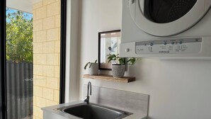 A modern kitchen with a built-in sink, a washing machine, and a window with a view of trees. - Mid-century Elegance in a leafy garden (Padbury)