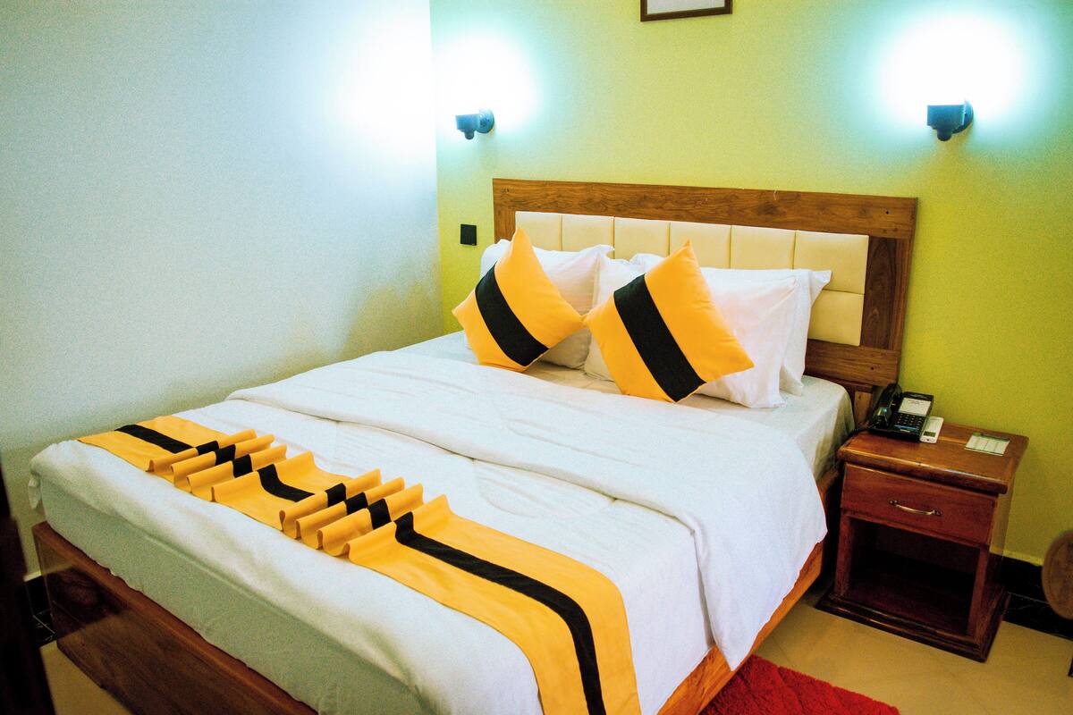 A hotel room with a bed, bedside table, and a nightstand with a phone.