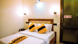 Une chambre d’hôtel avec un lit, une table de chevet, un téléphone, une porte avec une indication « pousser/tirer » et une paire de chaussons posés sur le sol.