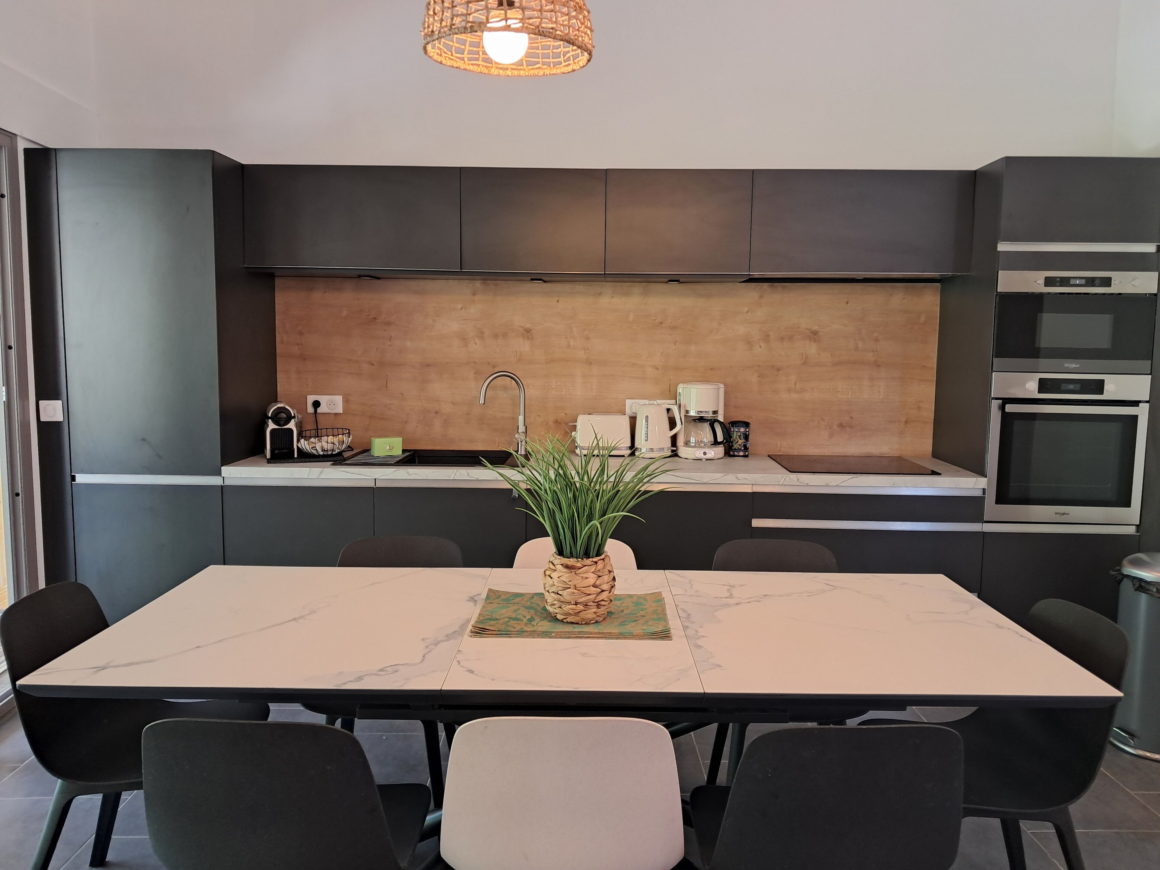 A modern kitchen with dark cabinetry, a marble countertop, and a dining area with a table and chairs.