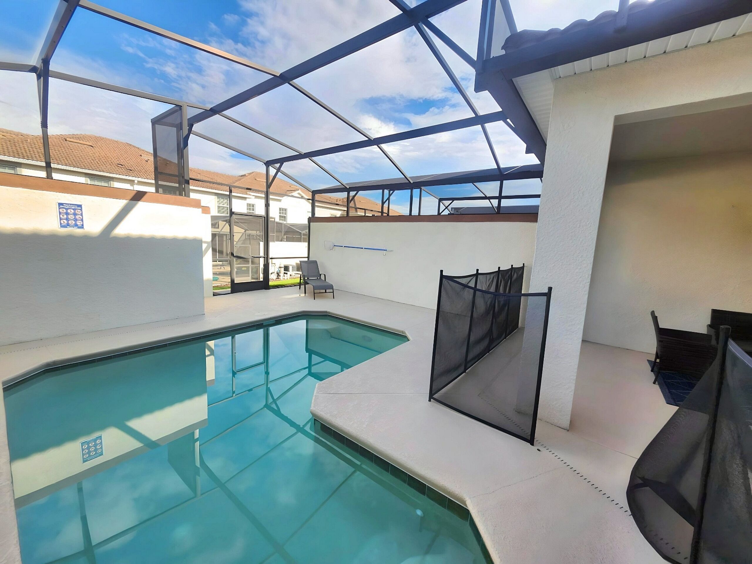 A swimming pool with a glass enclosure, a chair, and a fence.