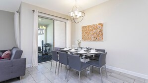 A dining area with a table set for four, grey chairs, a chandelier, and a modern abstract painting on the wall.