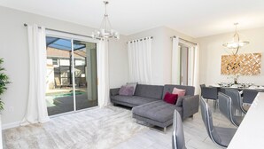 A modern living room with a grey sectional sofa, a fluffy rug, and a dining area with chairs and a table.