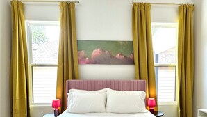 A hotel room with a large bed, two bedside lamps, a painting on the wall, and yellow curtains. - Charming 3-bedroom farmhouse in Wimberley with AC, WiFi (Wimberley)