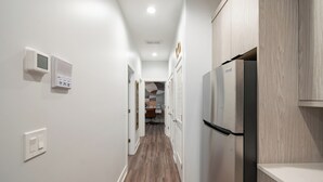 A narrow hallway with a wooden floor, white walls, and a stainless steel refrigerator on the right. - NEW Eco Stay by UChicago, Lakefront & Hyde Park! (Chicago)