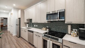 A modern kitchen with light wood cabinetry, a stainless steel microwave, a black stovetop, and a coffee maker. - NEW Eco Stay by UChicago, Lakefront & Hyde Park! (Chicago)