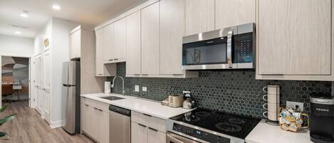 Una cocina moderna con armarios de madera clara, un microondas de acero inoxidable, una estufa negra y una cafetera.