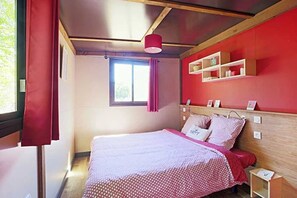 Un dormitorio con cama, una ventana con cortinas, una pared roja y una estantería con objetos.