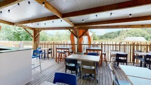 Une terrasse extérieure avec des tables et des chaises en bois, des guirlandes lumineuses et une vue sur le paysage environnant.