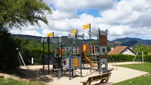 Un terrain de jeux avec des structures d’escalade et un banc, situé dans un parc avec une montagne en arrière-plan.