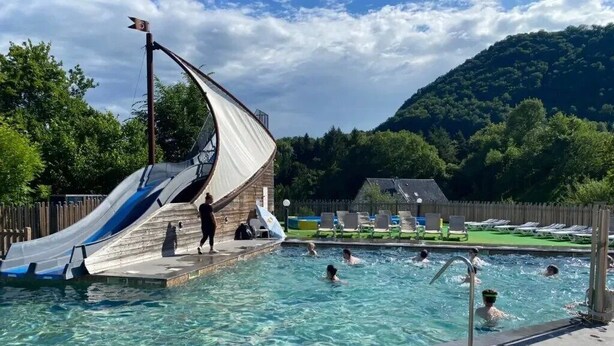 Une piscine avec un toboggan, entourée de chaises longues et d’une terrasse en bois.