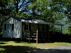 Uma cabana pequena com varanda, cercada por árvores e com uma montanha ao fundo.
