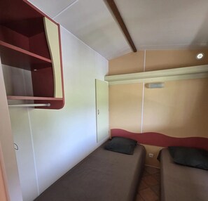 A compact room with a bunk bed, a small table, and a wall-mounted shelf. - ZEcamping 4* familial piscine couverte pet friendly mobil-home 22m2 (Vic-sur-Cère)