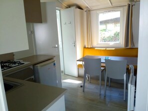A compact kitchen with a gas stove, a small refrigerator, and a dining area with two chairs and a table. - ZEcamping 4* animé piscine couverte pet friendly locatif TV 24m2 (Vic-sur-Cère)