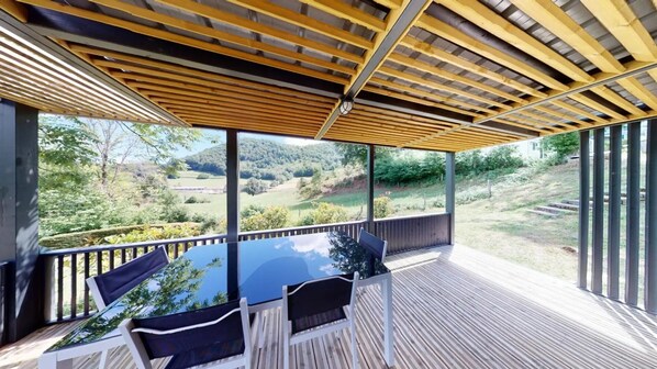 A covered outdoor seating area with a table and chairs, overlooking a scenic landscape. - ZEcamping 4 étoiles piscine couverte dog friendly animations chalet TV (Vic-sur-Cère)