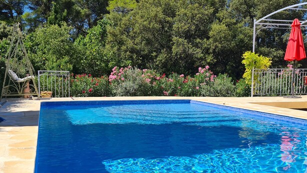 Une piscine rectangulaire à l’eau d’un bleu cristallin, entourée d’une terrasse carrelée et d’une clôture en métal.