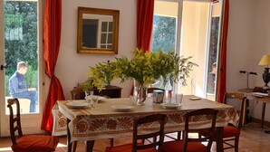 Un coin repas avec une table dressée pour quatre personnes, entourée de chaises, un vase de fleurs jaunes et un miroir au mur.