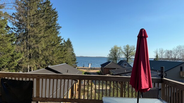 Une terrasse en bois avec une table et des chaises, donnant sur un lac, avec des maisons et des arbres en arrière-plan.