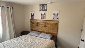 Une chambre avec une tête de lit en bois, un lit recouvert d’une literie à motifs, une petite table ronde et trois œuvres d’art murales sur le thème du cheval.