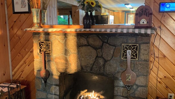 A stone fireplace with a mantel, a clock, and a vase with flowers. - Bootjack Lake House: Private Lakefront in the Heart of the Keweenaw (Lake Linden)
