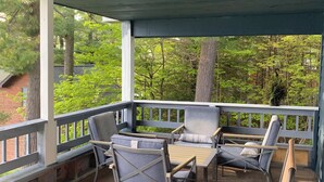 A covered patio with outdoor furniture, including chairs and a table, surrounded by a railing. - Bootjack Lake House: Private Lakefront in the Heart of the Keweenaw (Lake Linden)