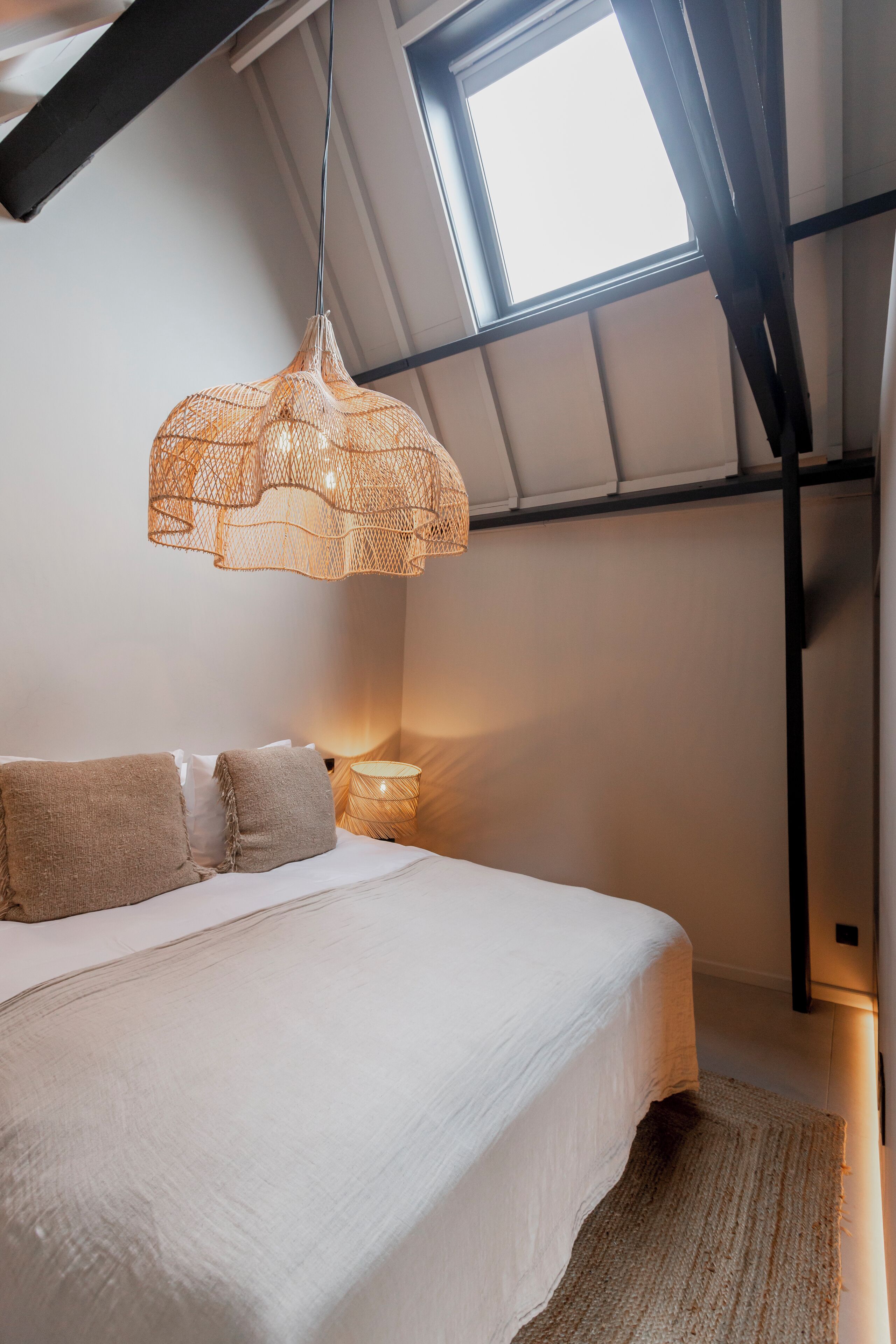 Une chambre à coucher avec un lit, un luminaire suspendu, une table de chevet et une fenêtre.