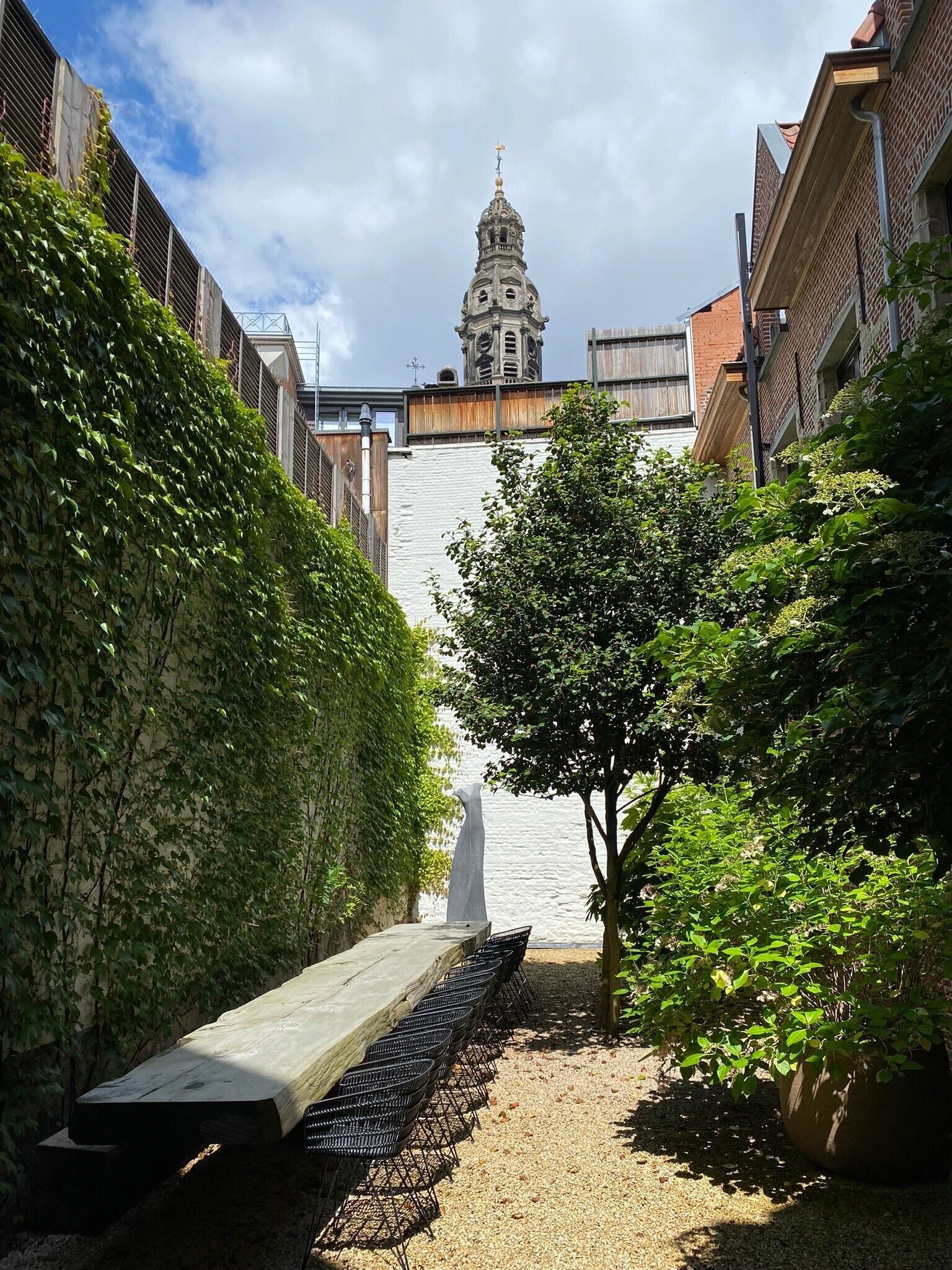 A narrow alley with a bench, greenery, and a distant clock tower.