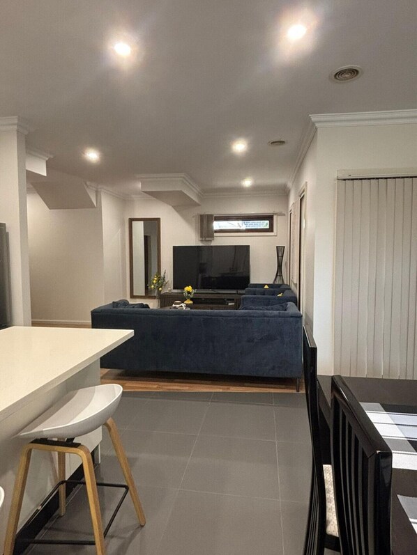 A modern living room with a sofa, a TV, and a dining area with a table and chairs.