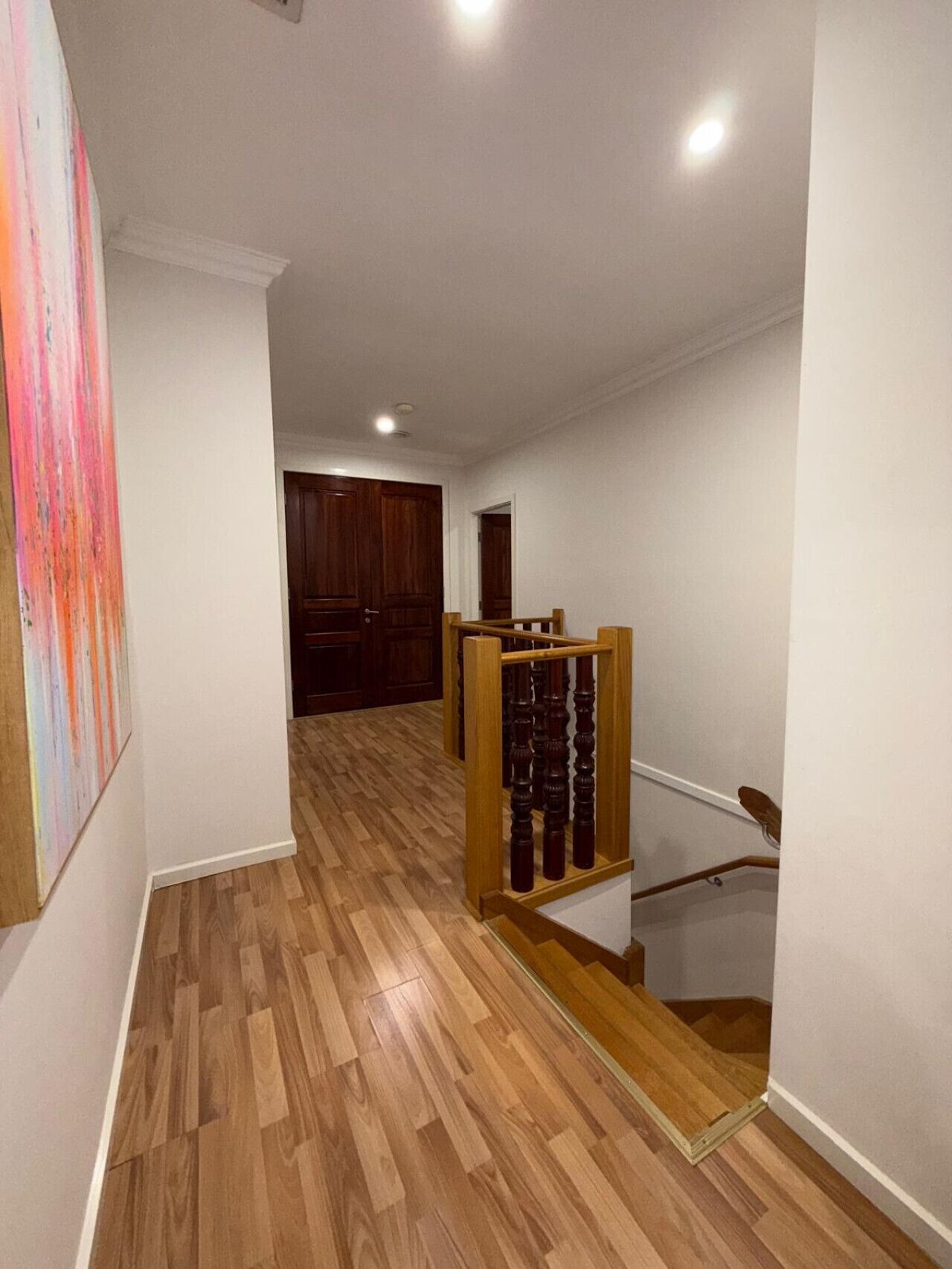 Un pasillo con suelo de madera, una escalera con barandilla de madera y una puerta al final.
