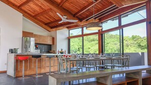 A modern kitchen with a large island, bar stools, and a dining area with a long table and chairs. - Villa Nou Cinq, jungle view, swimming pool and beach 5 min away (Le Gosier)