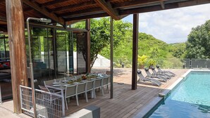 An outdoor pool area with a covered seating area, lounge chairs, and a view of the surrounding greenery. - Villa Nou Cinq, jungle view, swimming pool and beach 5 min away (Le Gosier)